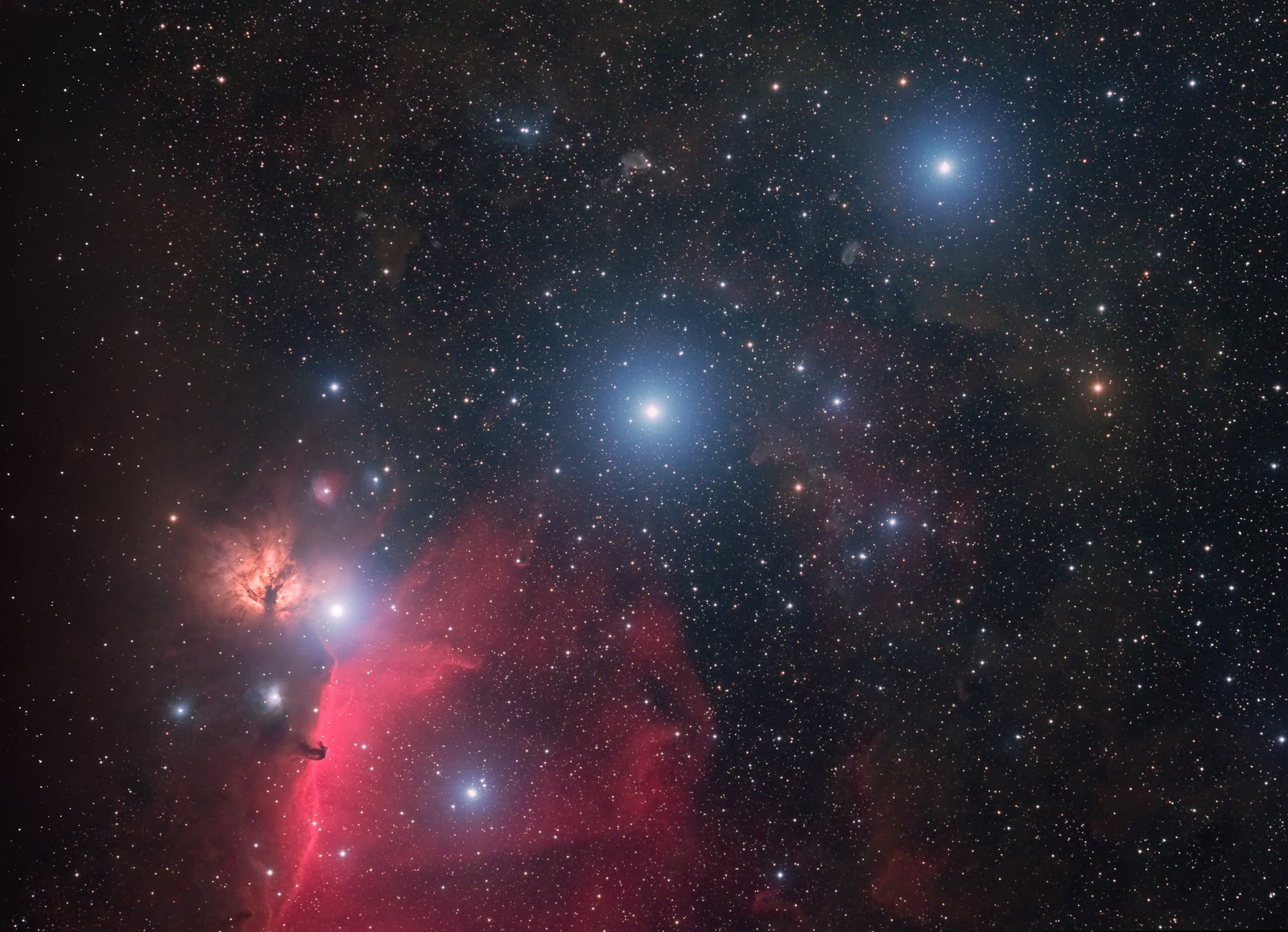 The three stars of Orion's Belt among glowing gas clouds: Alnilam is the bright blue star at the centre, with Alnitak at lower left beside the Flame and Horsehead Nebulae and Mintaka at upper right.