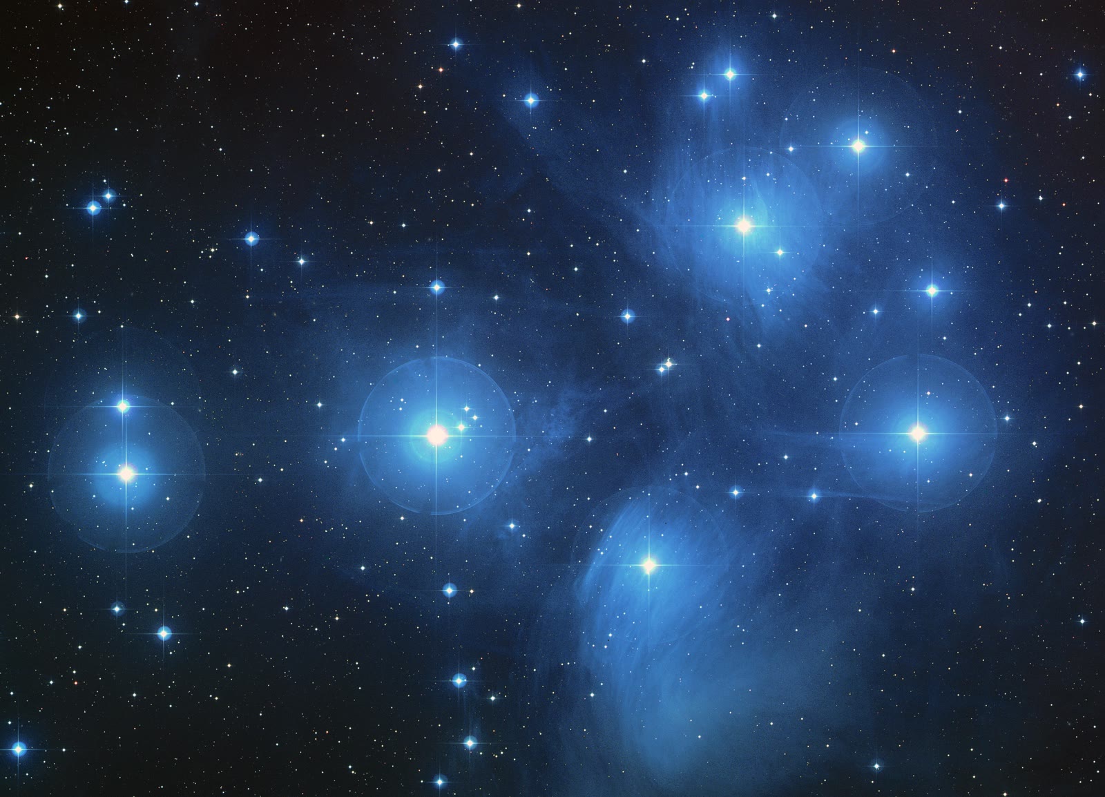 The Pleiades star cluster wrapped in blue reflection nebulosity, with Merope as the bright star below and right of centre, embedded in the wispy Merope Nebula.